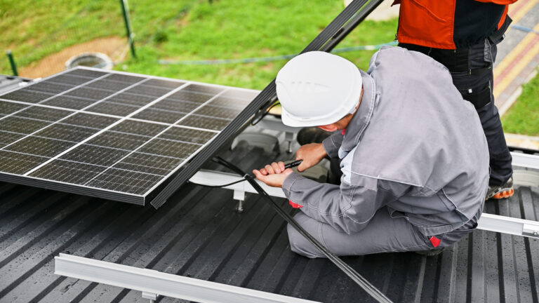 Mounters connecting cables while installing photovoltaic solar panels on roof of house. Workers mounting of PV solar modules on rooftop. Concept of alternative and renewable energy.