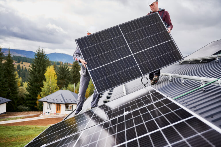 Technicians installing solar panel system on roof of house. Men Installers in helmets carrying photovoltaic solar module outdoors. Concept of alternative and renewable energy.